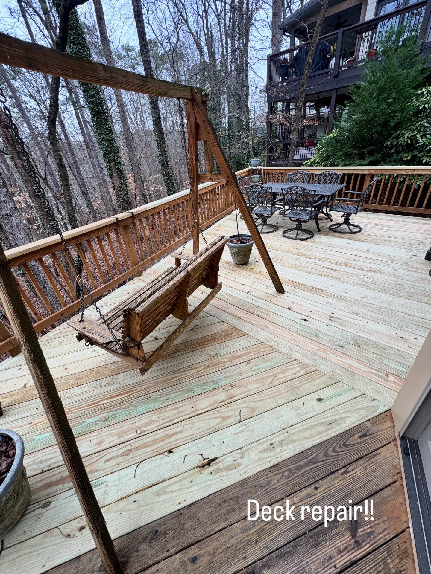 A wooden deck with a swing, featuring a section of new, lighter-colored replacement boards next to older, weathered wood.