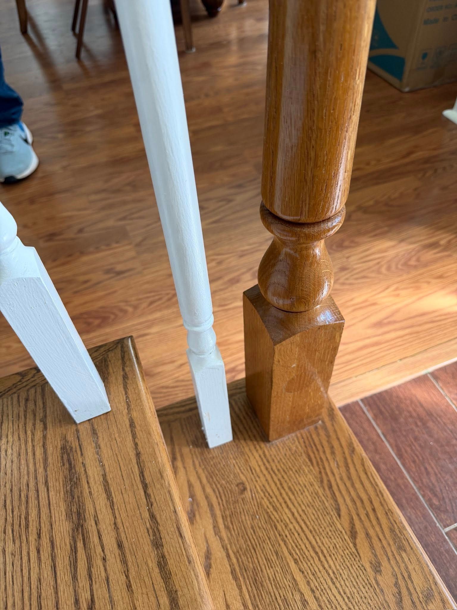 Close-up of a stair tread with two white wooden balusters and a larger, natural-finish oak newel post.