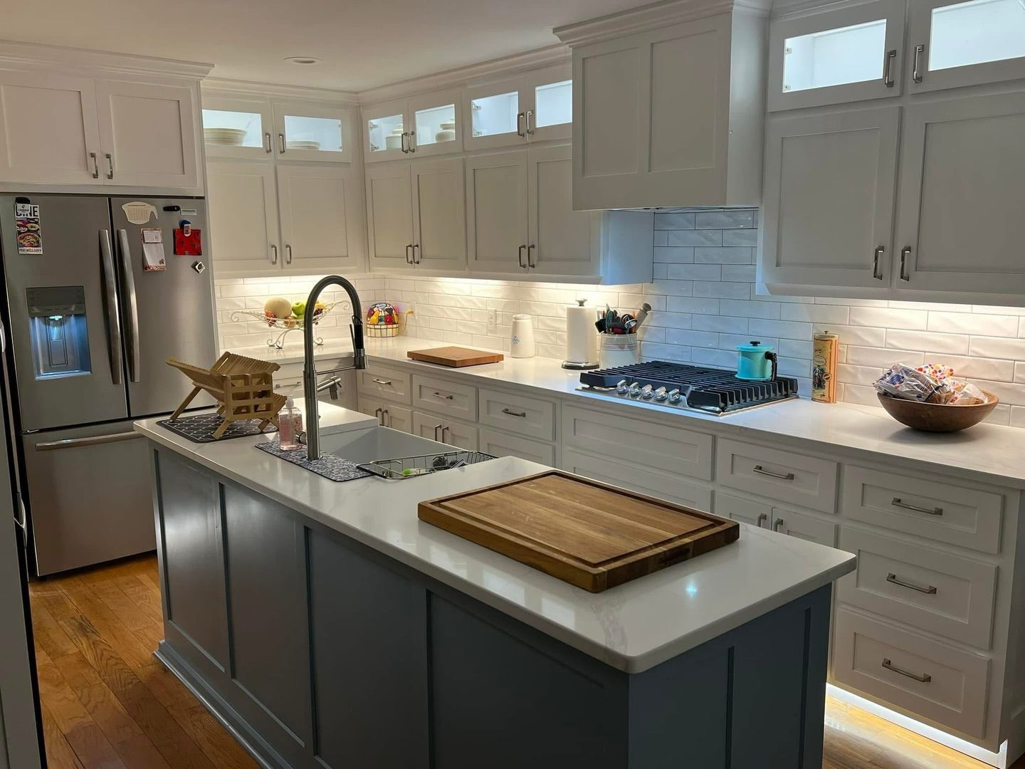 Modern kitchen with white upper cabinets, light-gray island, stainless steel appliances, and under-cabinet lighting.