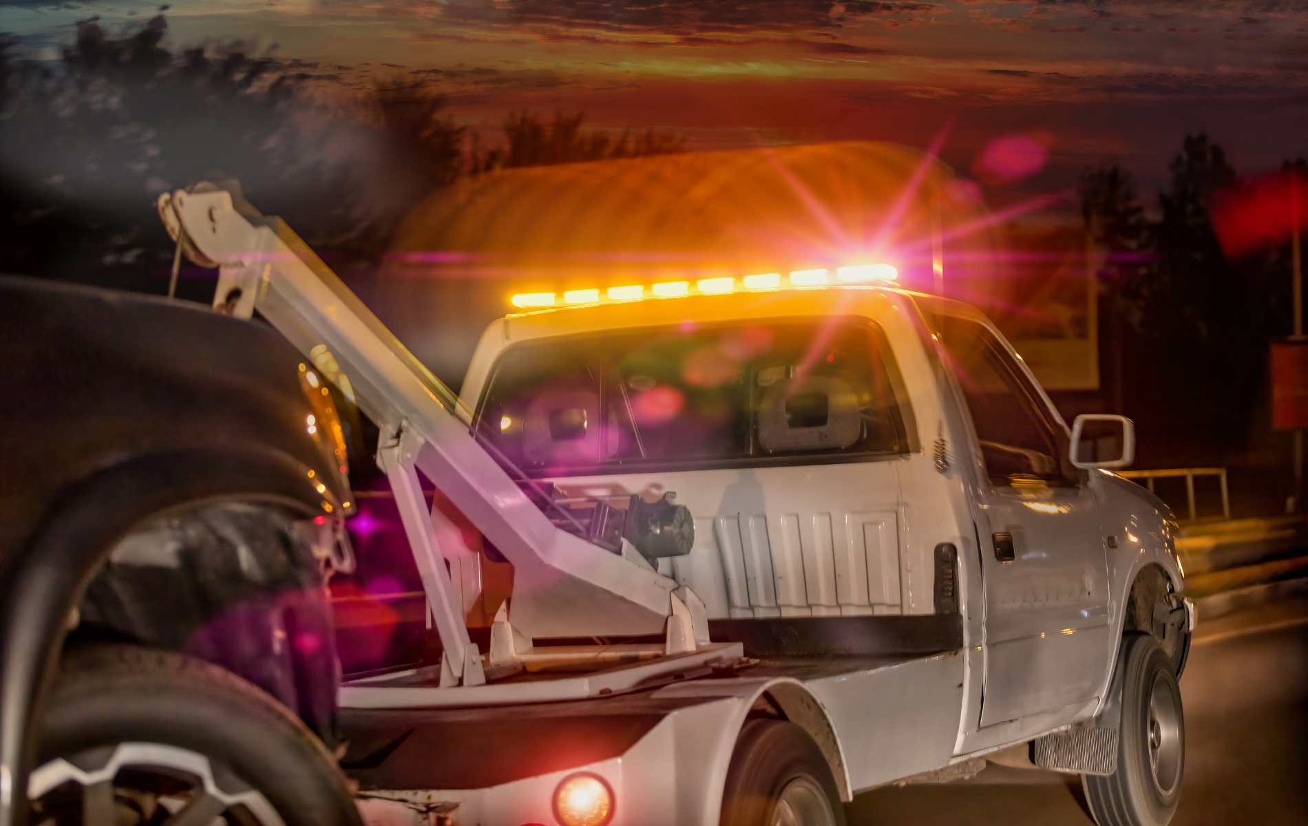 A tow truck is towing a car on the side of the road at night.