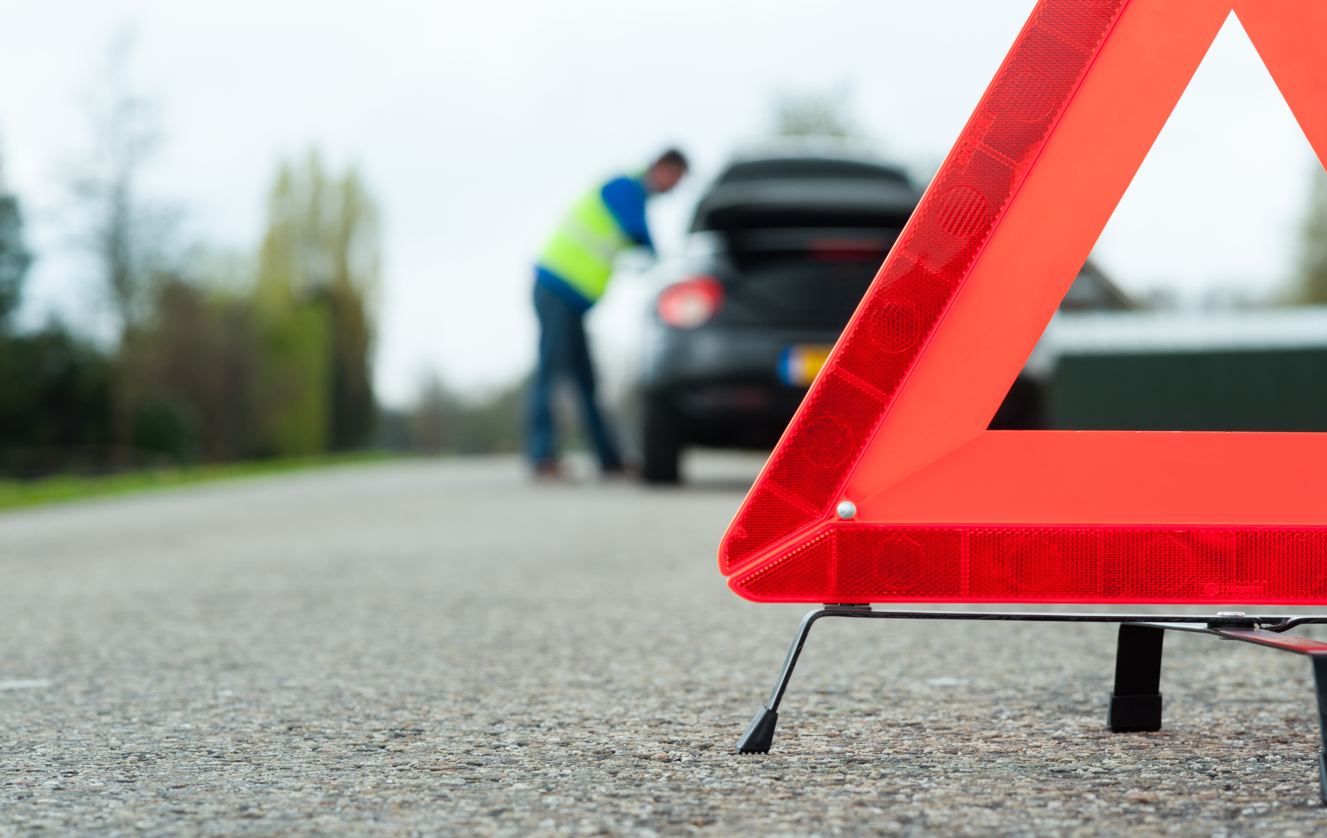 A man is standing next to a broken down car on the side of the road.