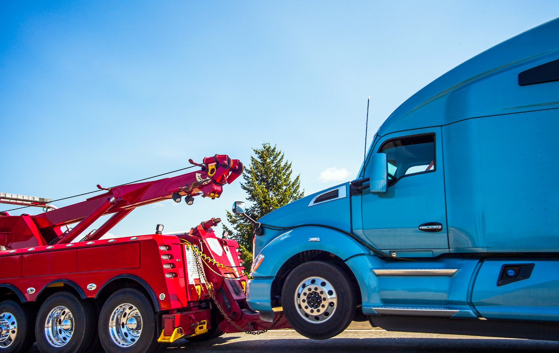 A blue semi truck is being towed by a red tow truck.