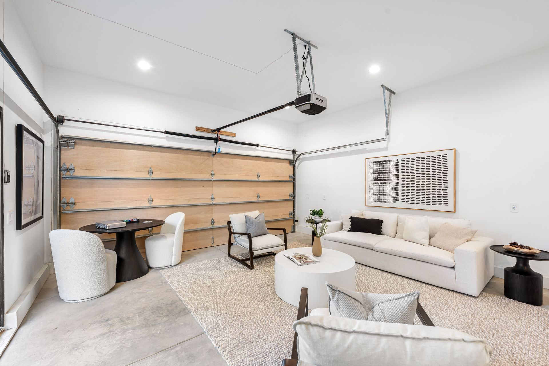 Living room conversion in a garage with furniture, white walls, and a wooden garage door.