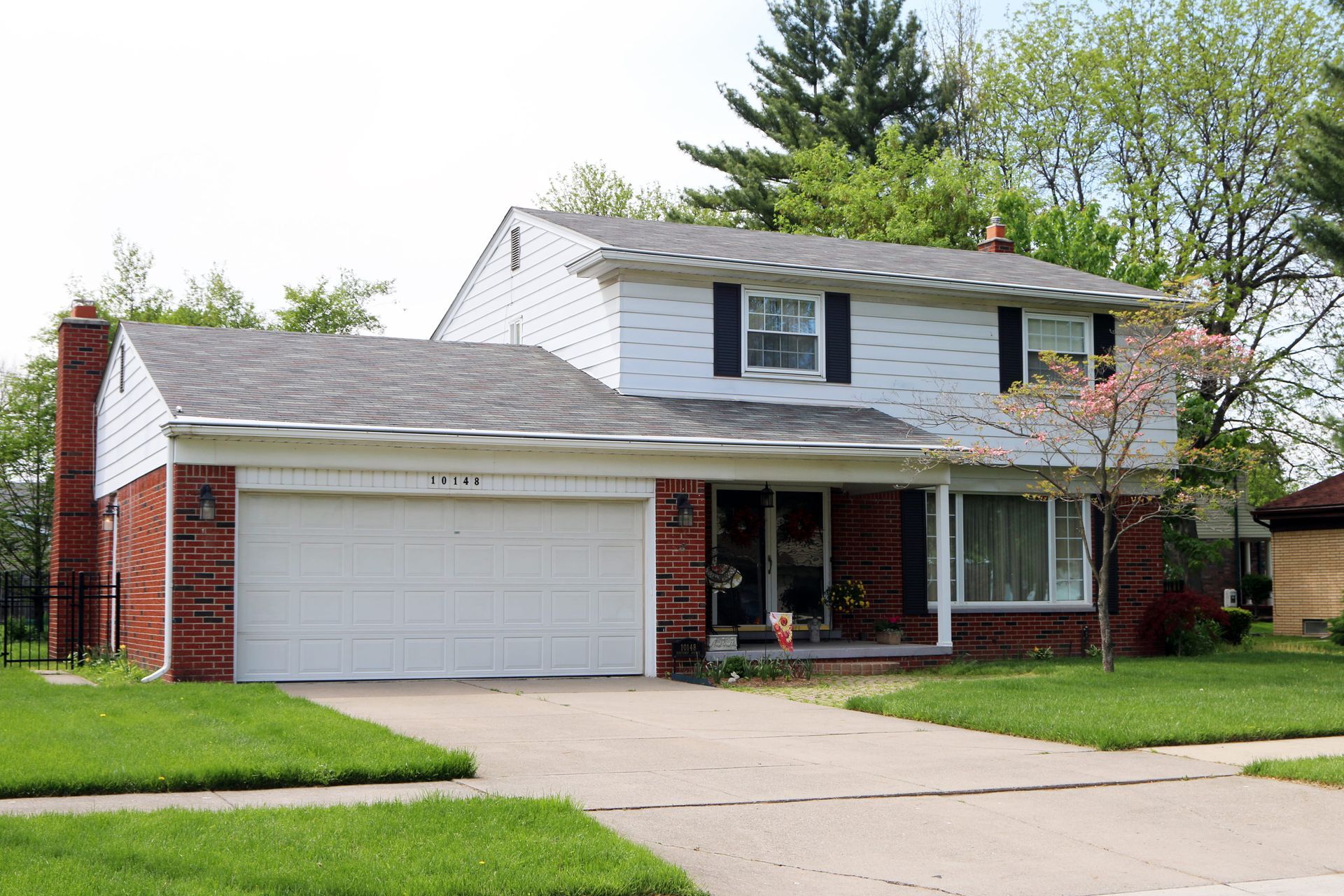 Two-story brick and white house with attached garage, green lawn, and driveway.