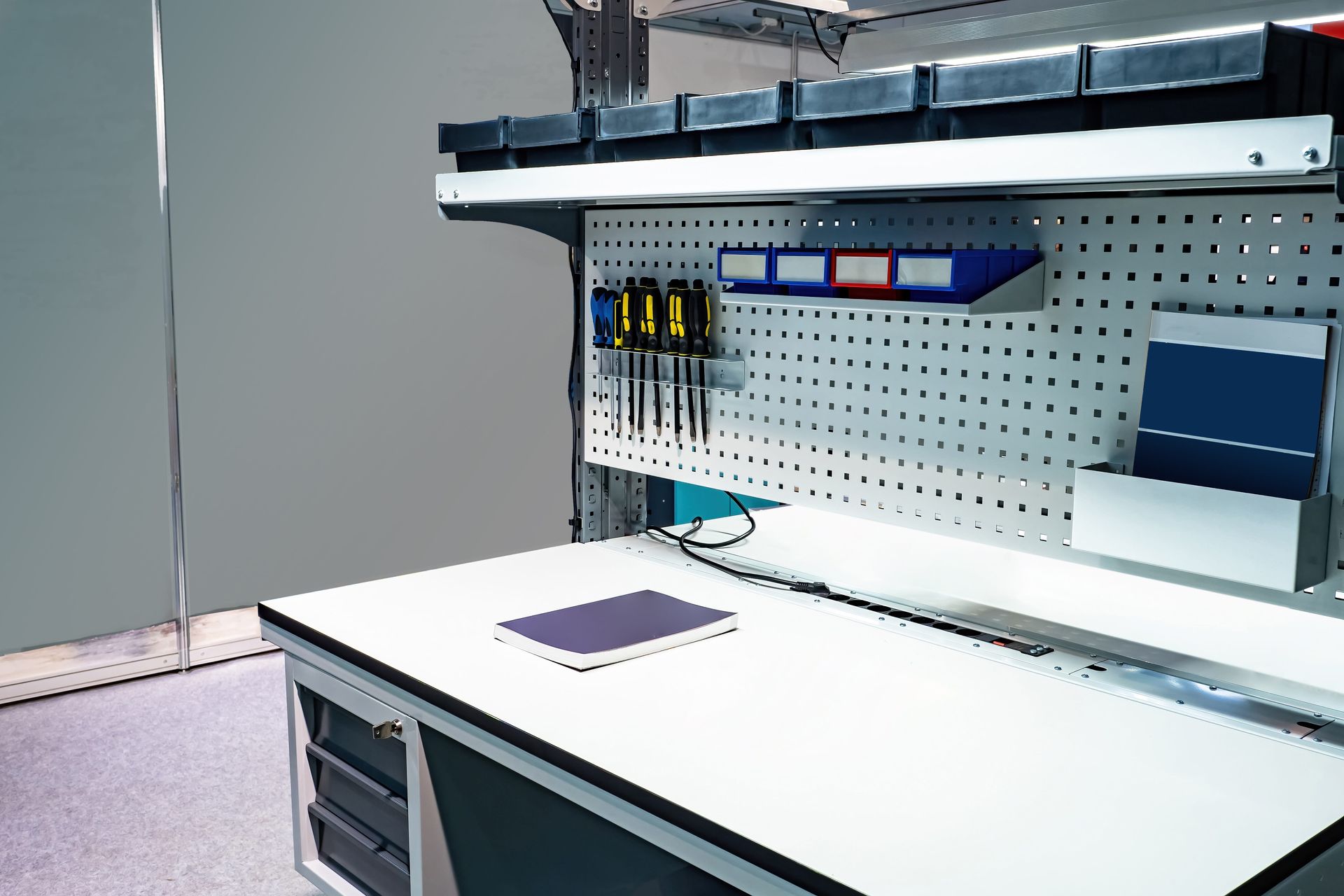 Workshop with white workbench, pegboard, tools, storage bins, and a notebook.