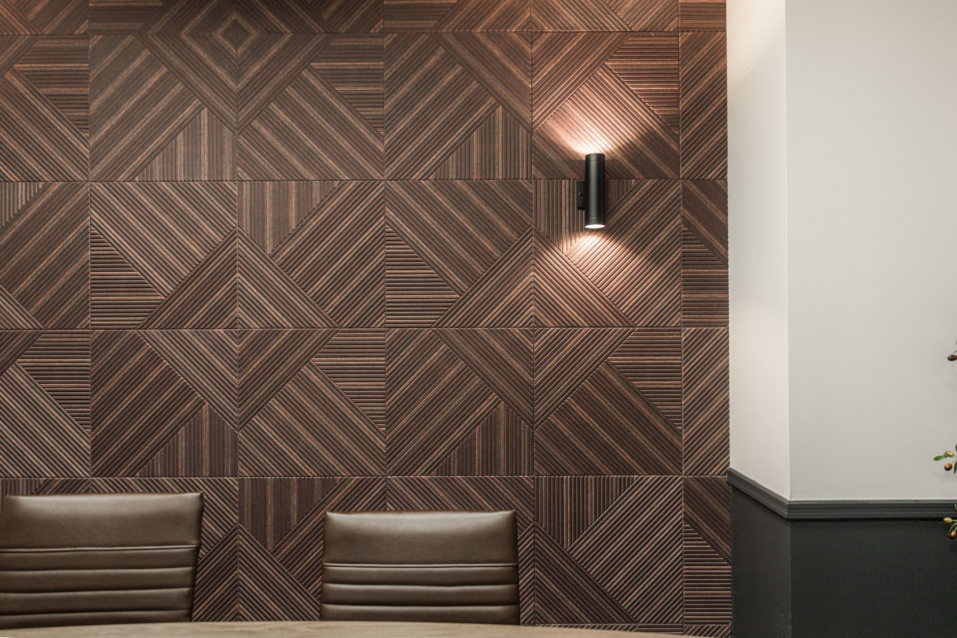 Brown geometric-patterned wall with benches and a wall sconce in a modern interior.