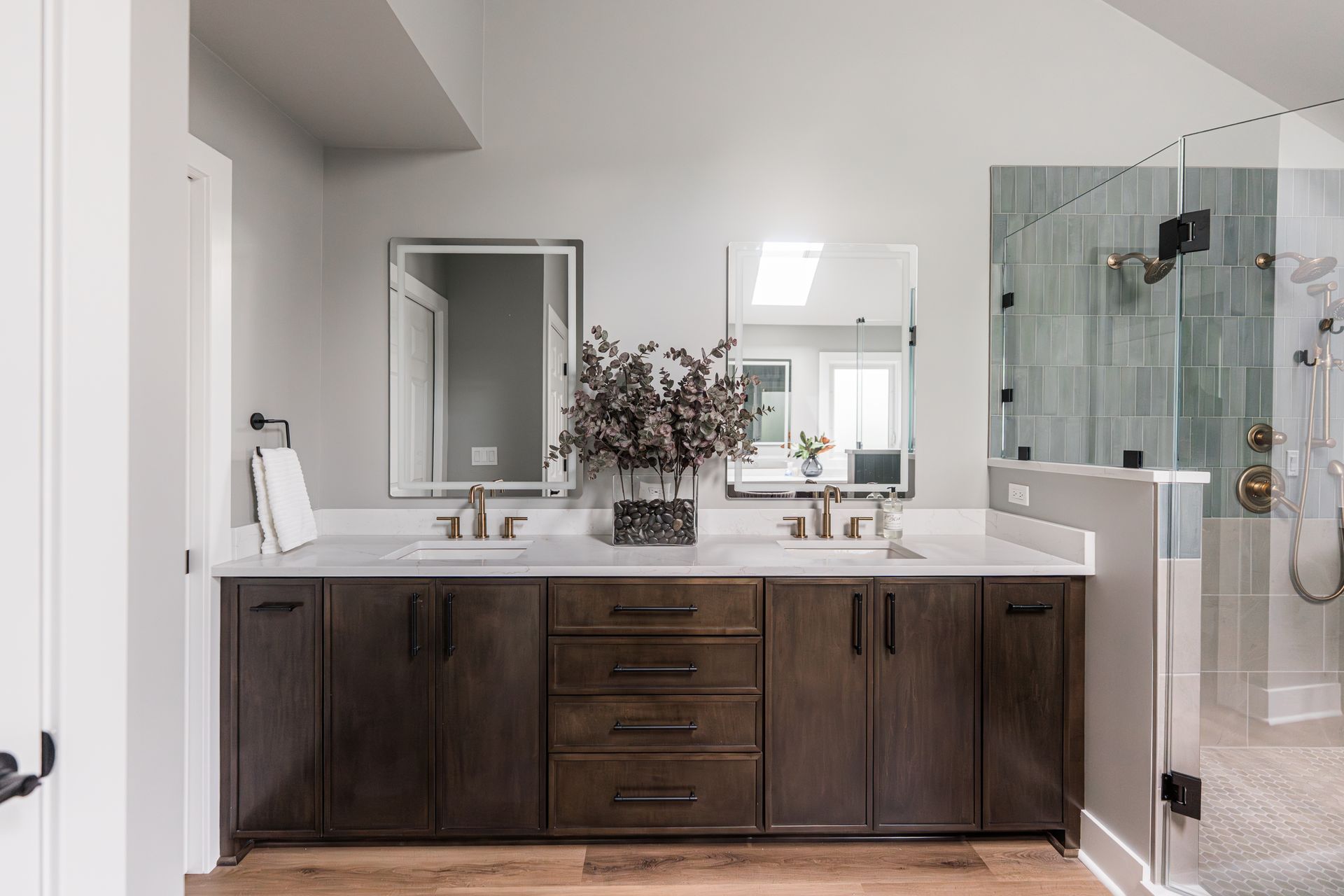 Modern bathroom with dark wood vanity, double sinks, large mirror, and glass shower.