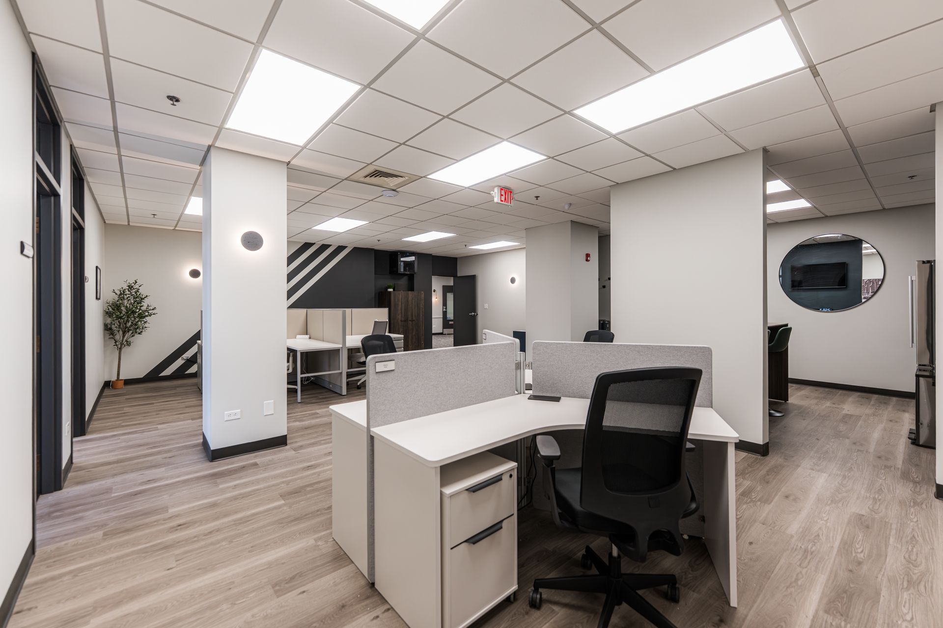 Modern office interior with cubicles, desks, black chairs, and wood-look flooring under bright ceiling lights