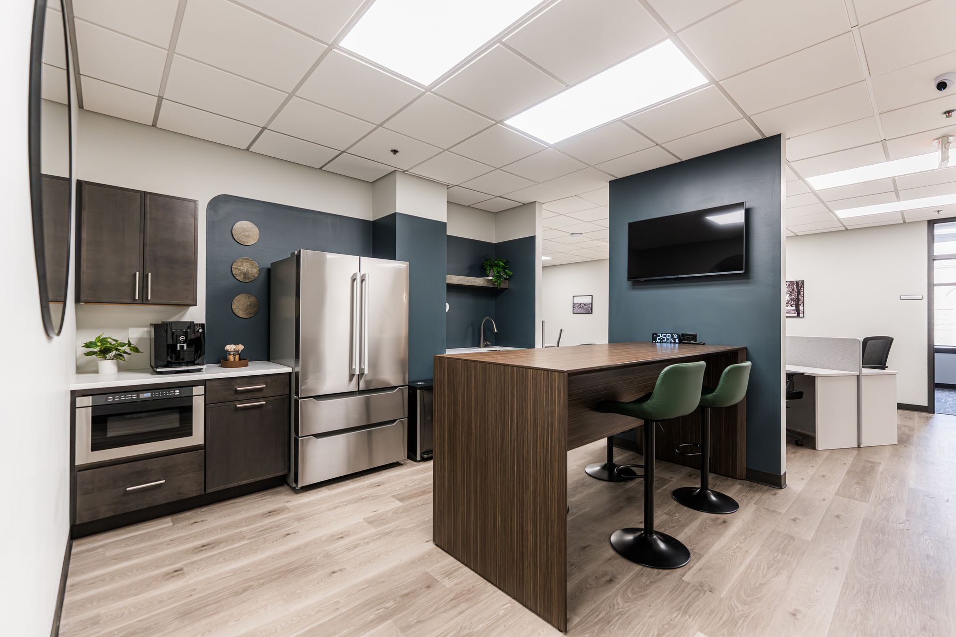 Modern office kitchenette with stainless steel appliances, dark cabinets, a wood island, and wall-mounted TV