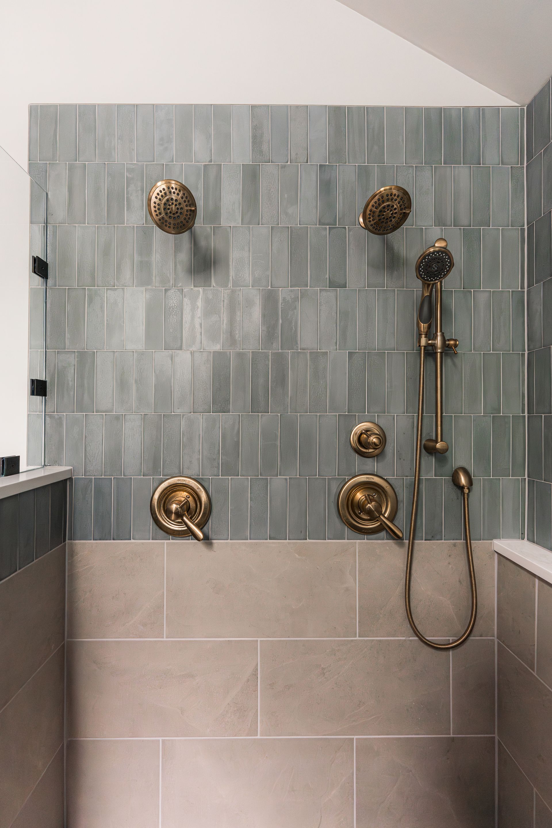 Luxury tiled shower with brass fixtures, gray wall tile, and beige lower tile panels.