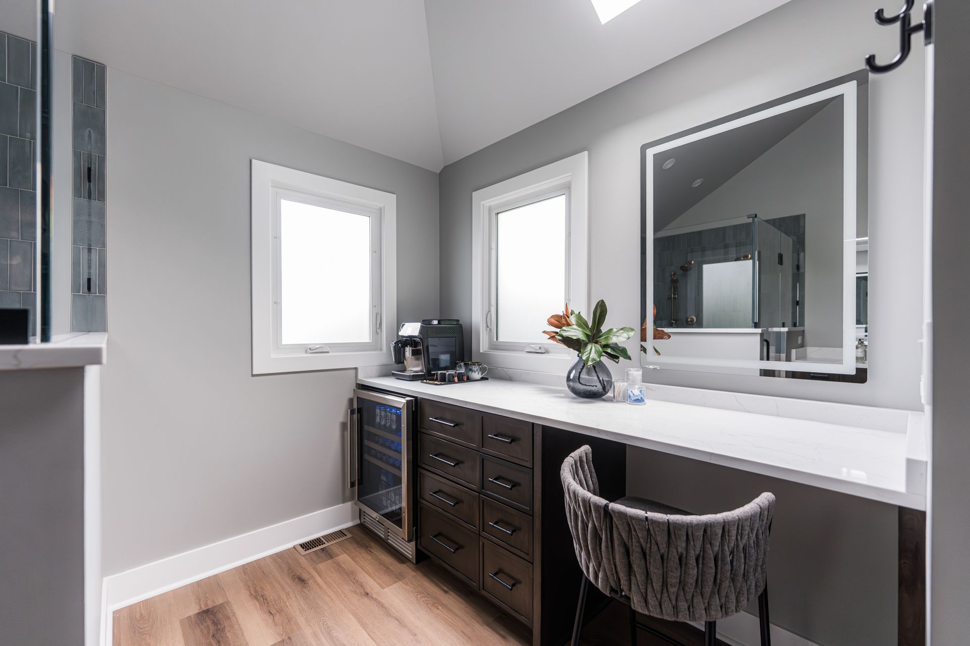 Modern gray home office with desk, chair, window, mirror, and small wine cooler under the counter.