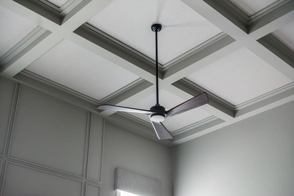 White coffered ceiling with a black ceiling fan in a softly lit room