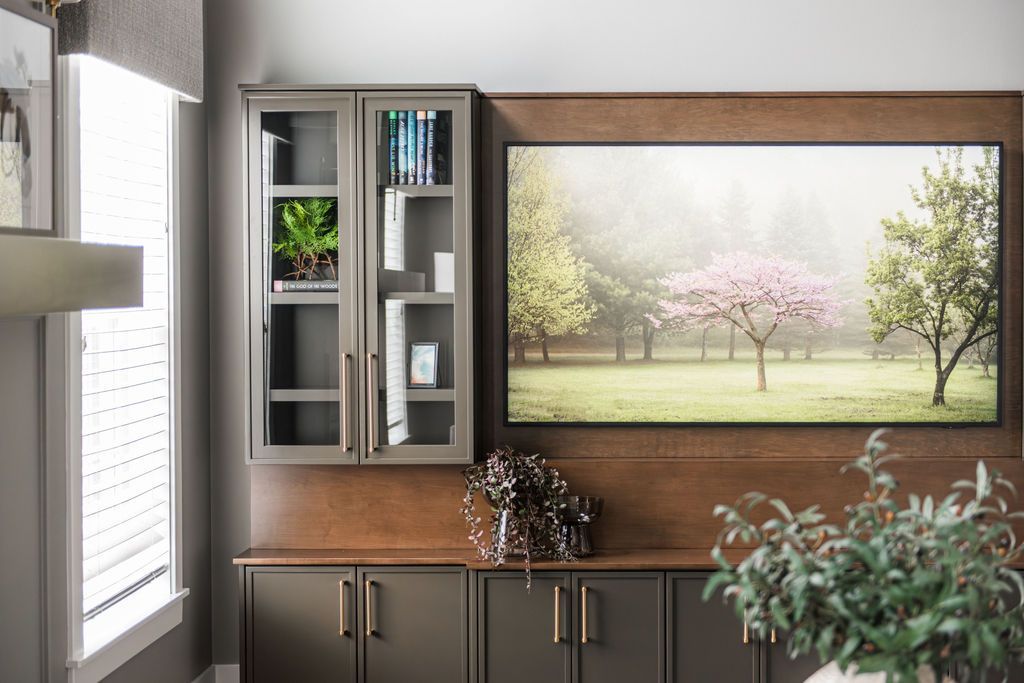 Modern living room with wall art, glass cabinet, and dark cabinets beneath a wood panel wall