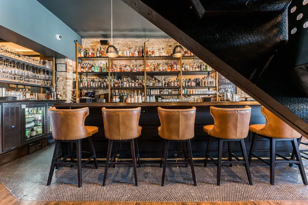Bar with leather bar stools and shelves of liquor bottles.