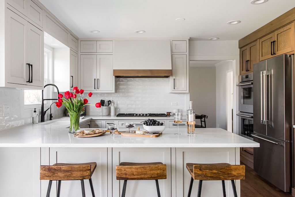 Modern kitchen with white cabinets, island, and wooden accents, stainless steel fridge.