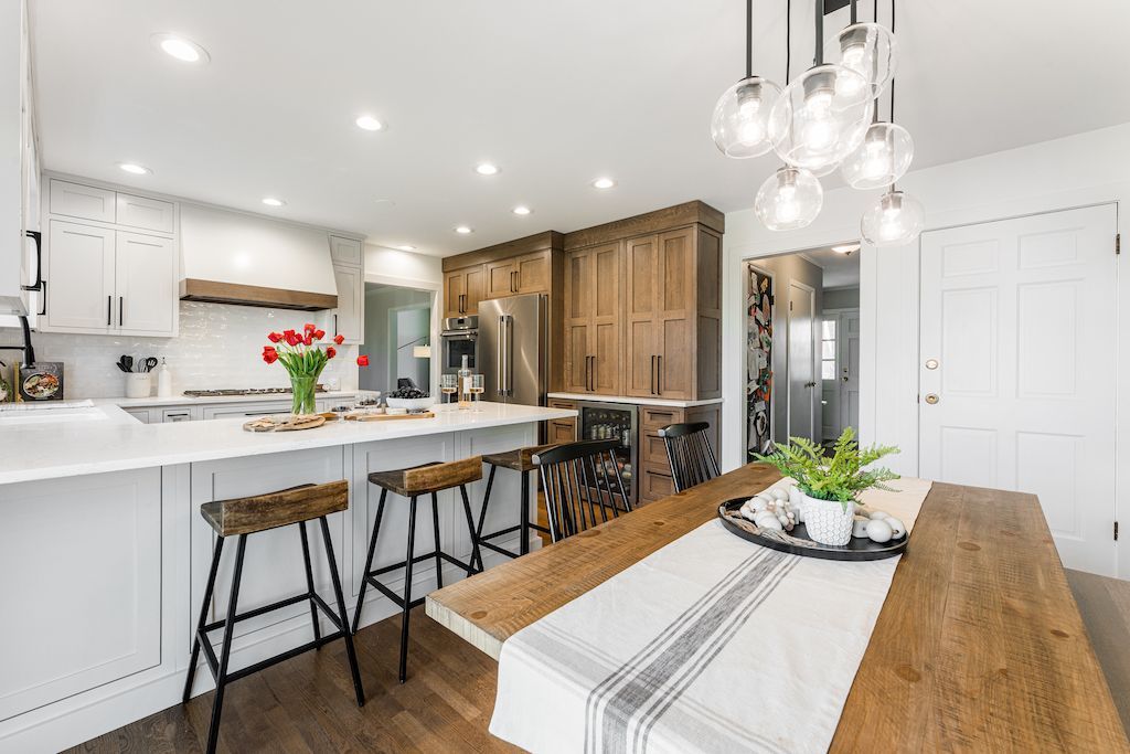 Modern kitchen with white and wood cabinetry, island with stools, and a dining table.
