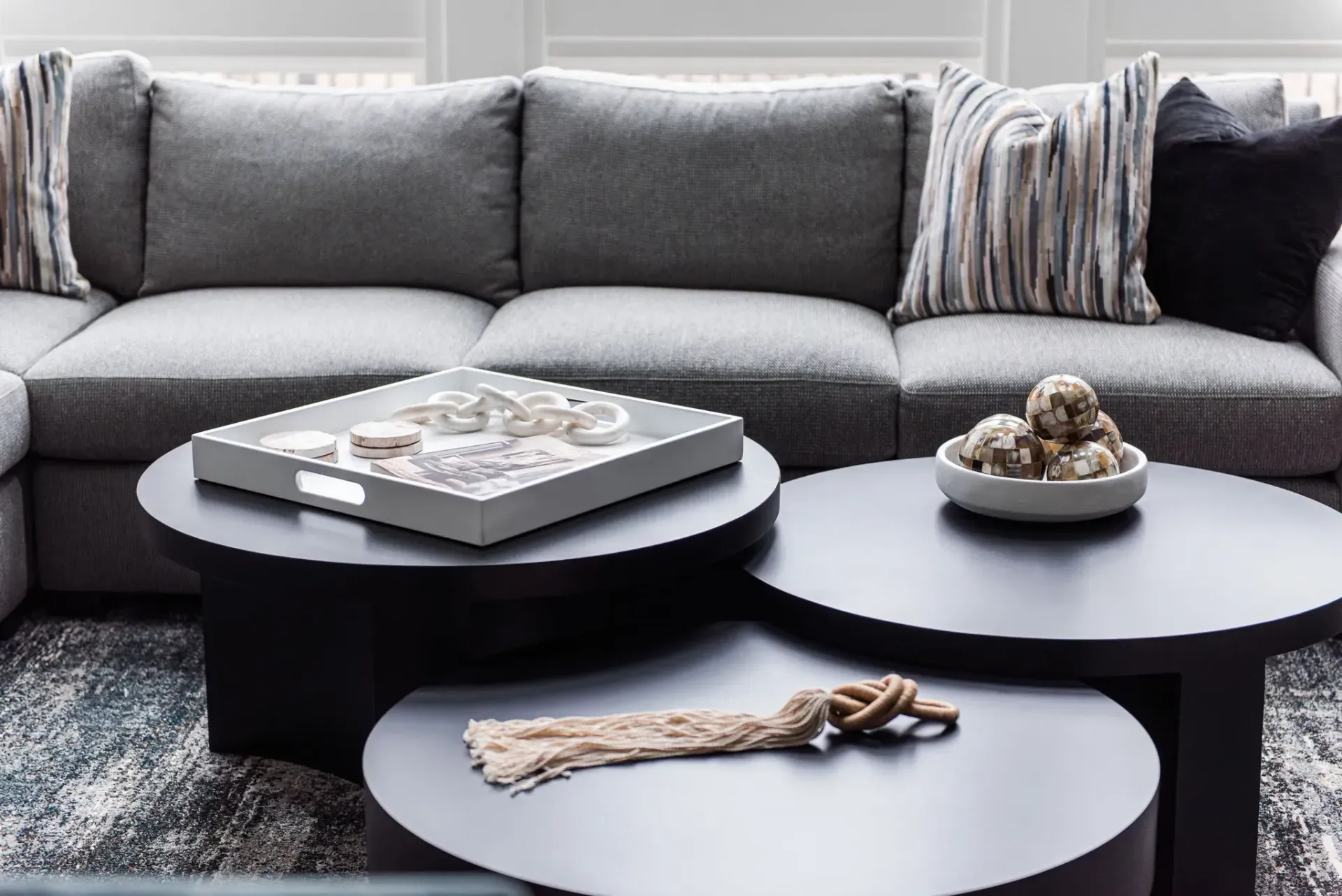 Gray sectional sofa with decorative pillows, three black round coffee tables, and rug.