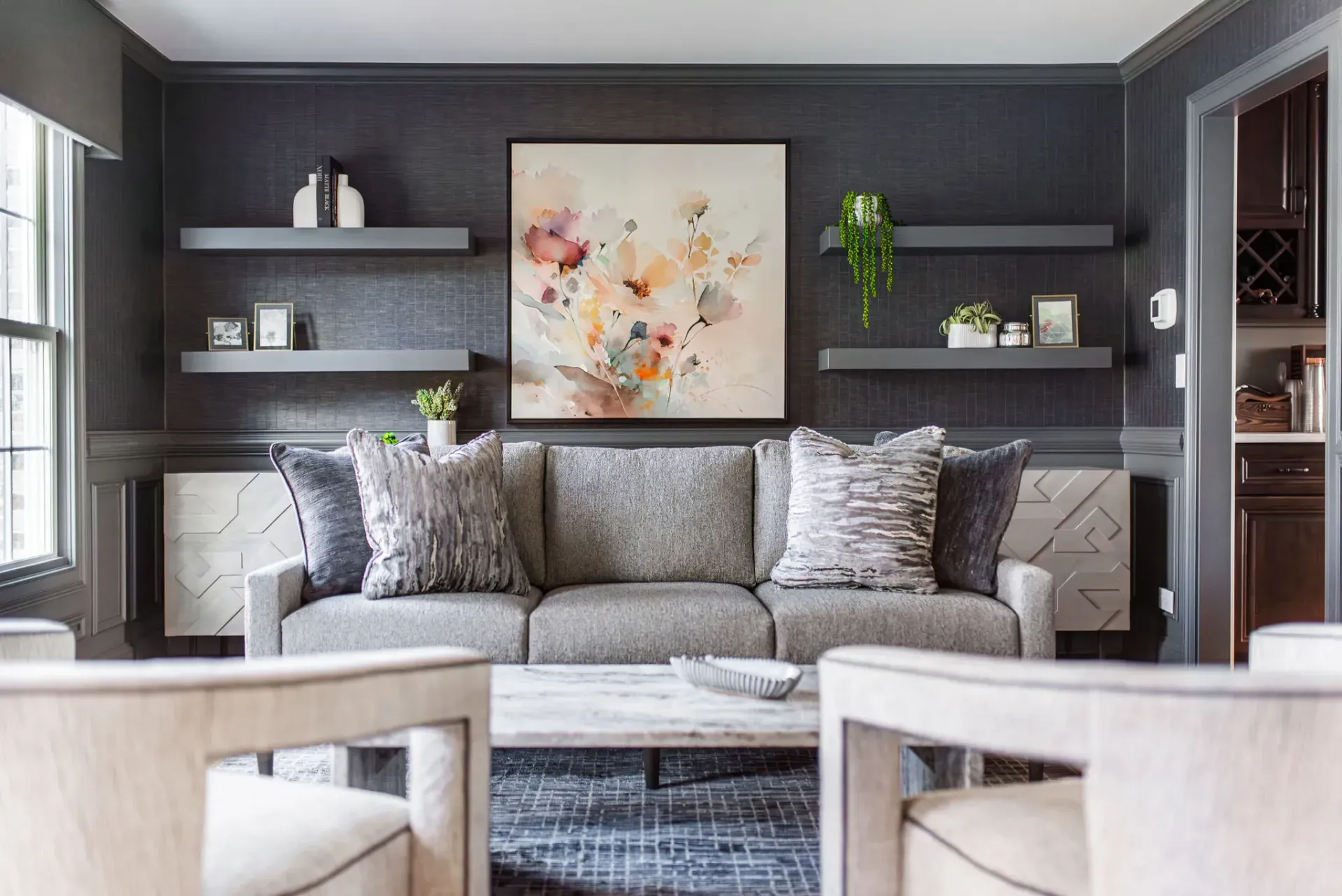 Gray living room with a sofa, floating shelves, art, and two armchairs.