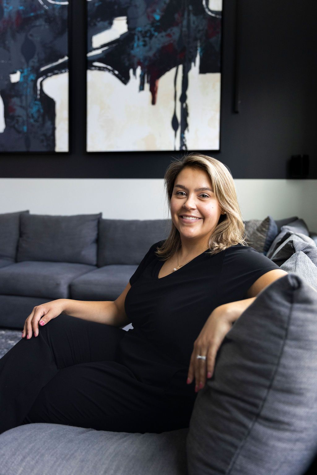Woman smiling on a gray couch in a room with abstract art.