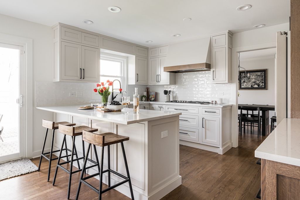 Modern white kitchen with island, wooden stools, and hardwood floors.