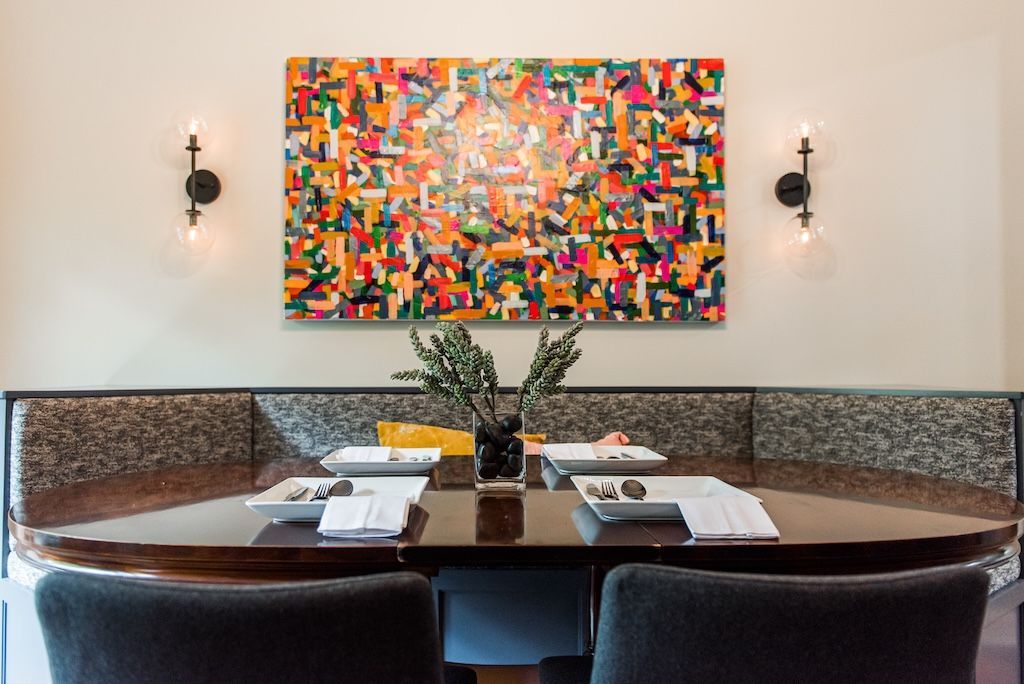 Dining area with a colorful abstract painting, a dark wood table, a built-in bench, and black sconces.
