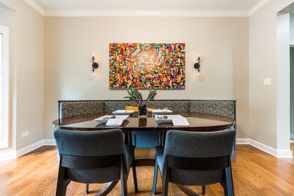 Dining room with wooden table, gray chairs, colorful artwork, and sconces.