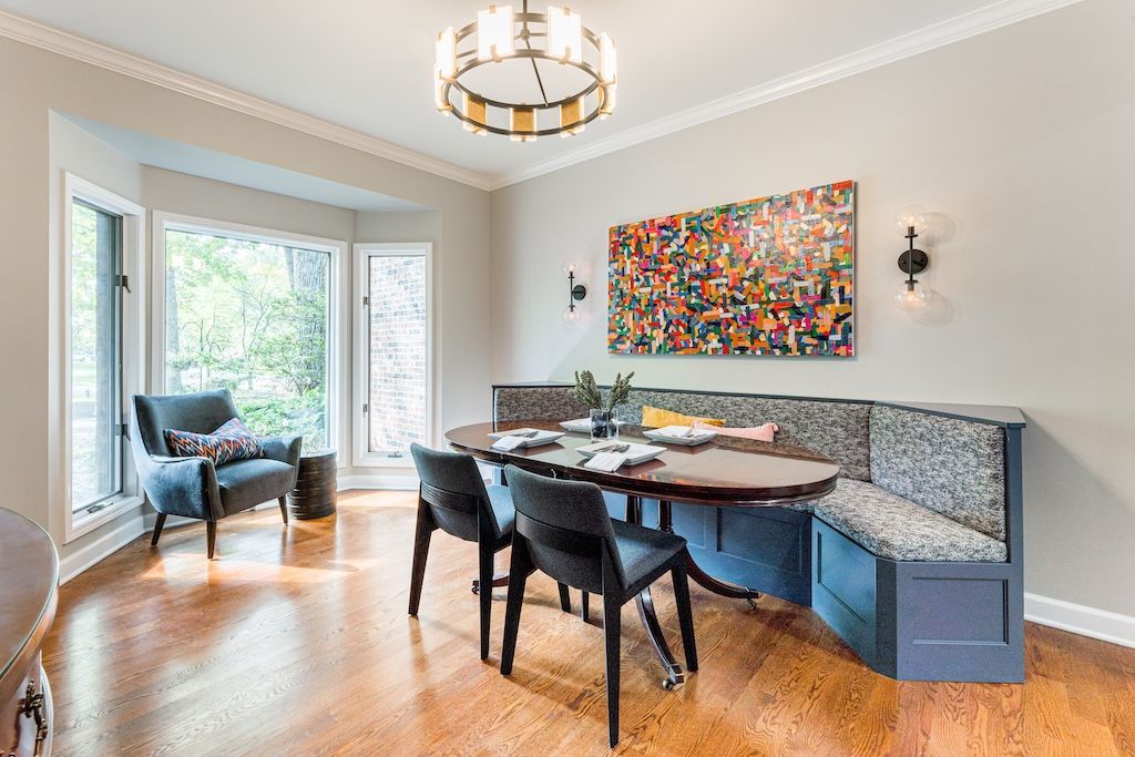 Dining room with round table, built-in blue bench, and black chairs. Colorful abstract art on the wall.