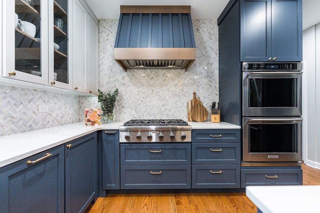 Blue kitchen with marble backsplash, stainless steel appliances, and wood floors.