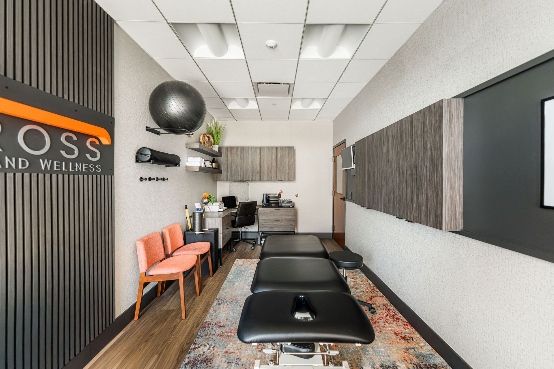 A modern chiropractic office with treatment table, chairs, desk, and exercise equipment.
