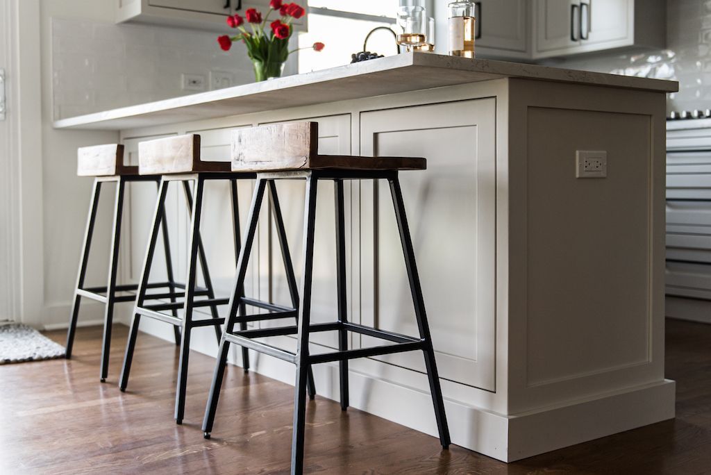 Kitchen island with three wooden-top bar stools, white cabinetry, hardwood floor, tulips on countertop.