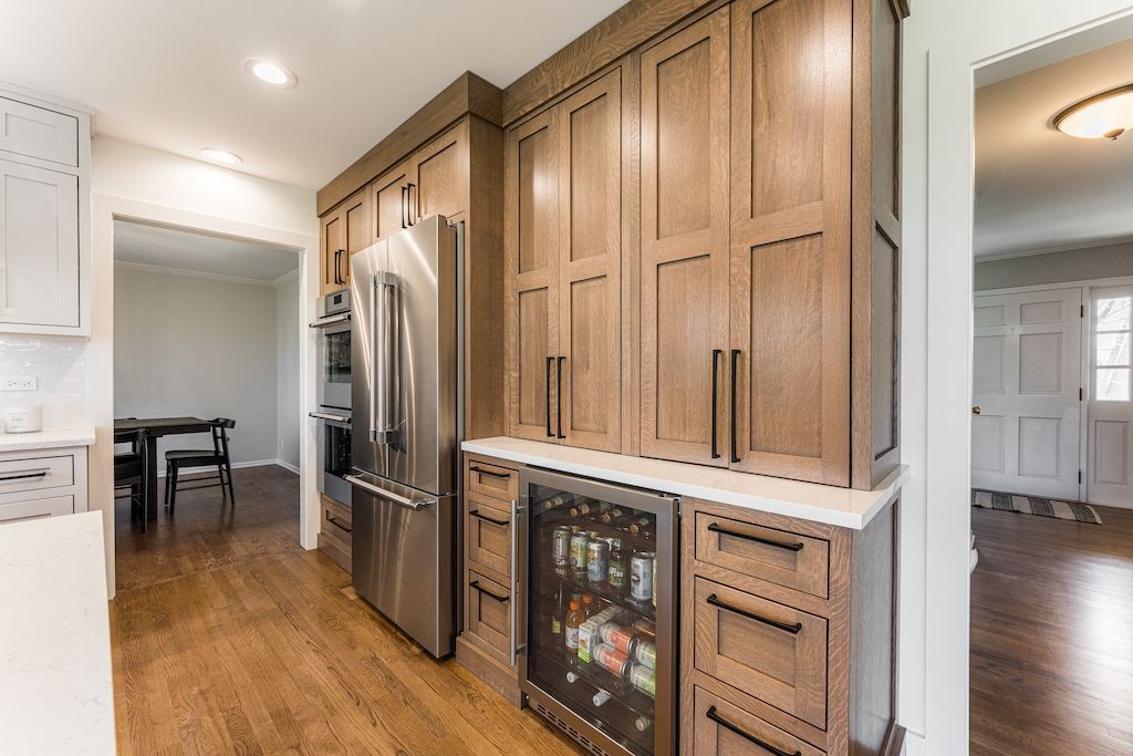 Kitchen with wooden cabinetry, stainless steel refrigerator, wine cooler, and hardwood floors.