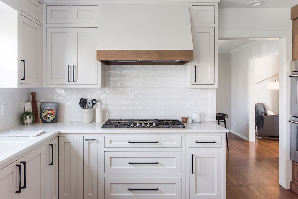 White kitchen with light wood range hood, white cabinets, and dark hardware.