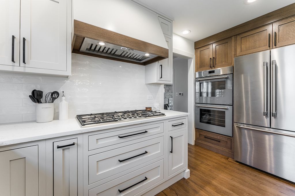 White kitchen with stainless steel appliances, wood accents, and gas cooktop.