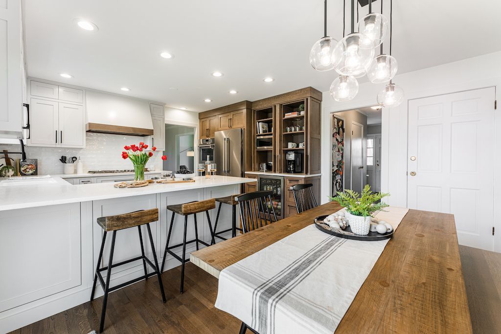 Modern kitchen with white cabinets, wood island and dining table, rustic stools, pendant lights.