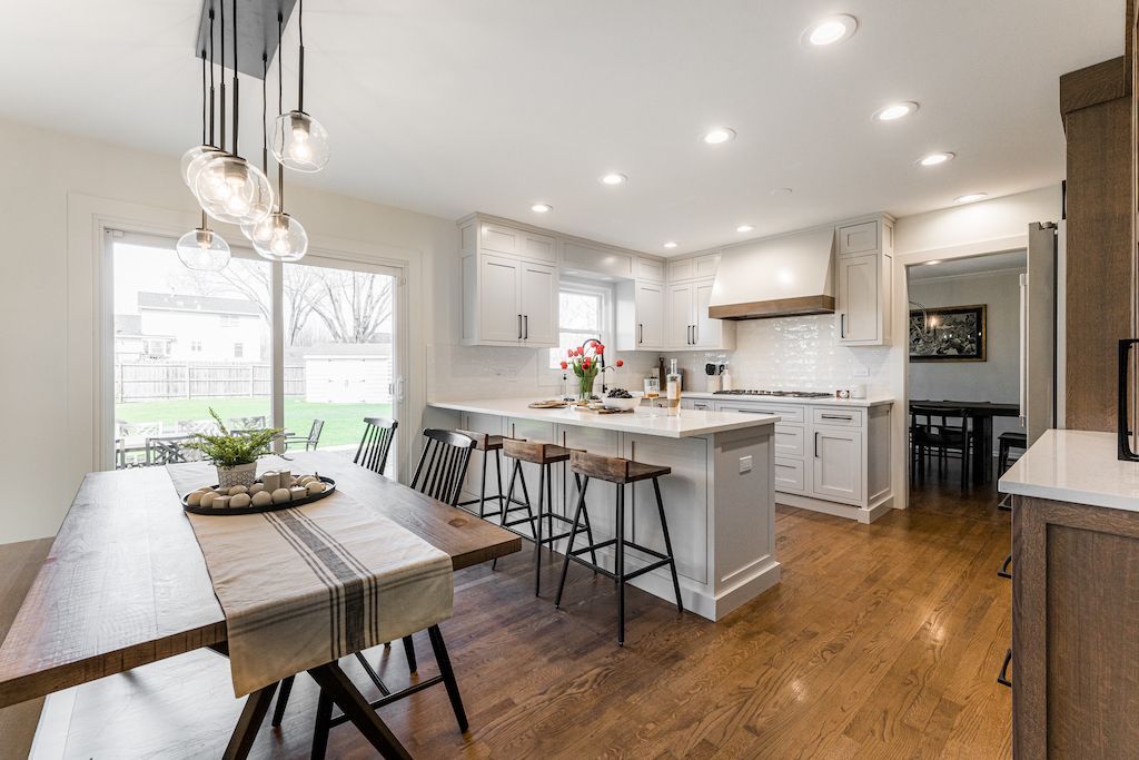 Modern kitchen and dining area with hardwood floors, white cabinets, and island with bar stools.