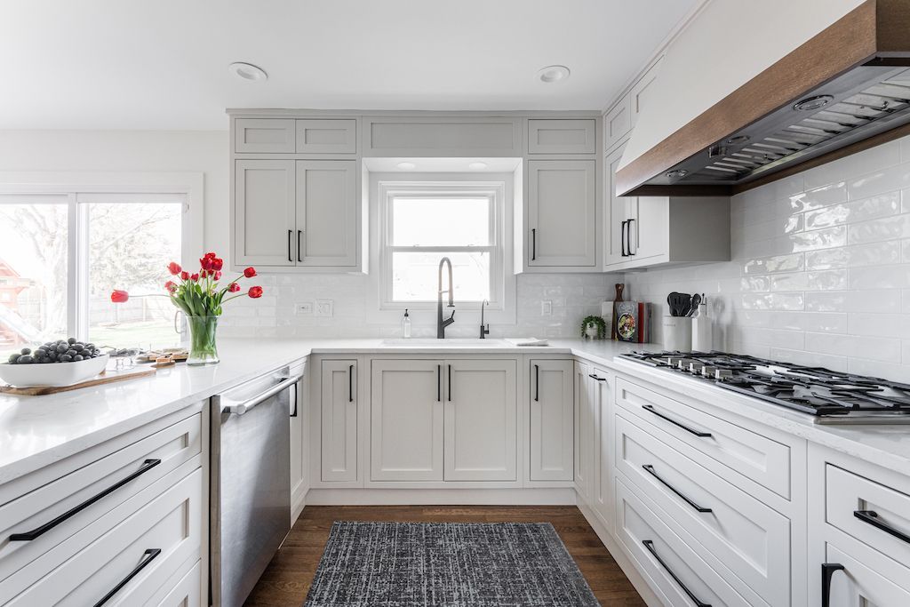 White kitchen with dark hardware, marble backsplash, and wooden accents.