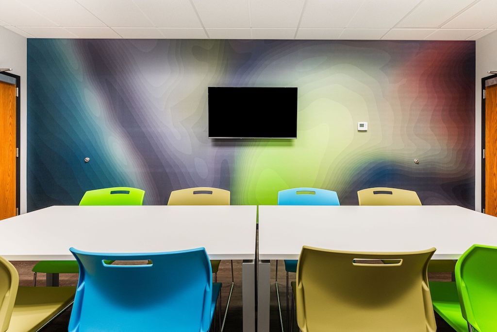 Conference room with a large white table, colorful chairs, a TV, and abstract wall art.
