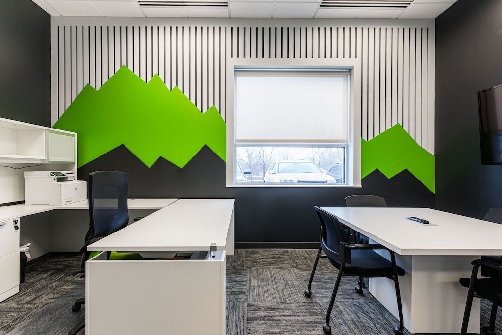 Modern office with white desks, black chairs, green mountain mural, and window with shade.