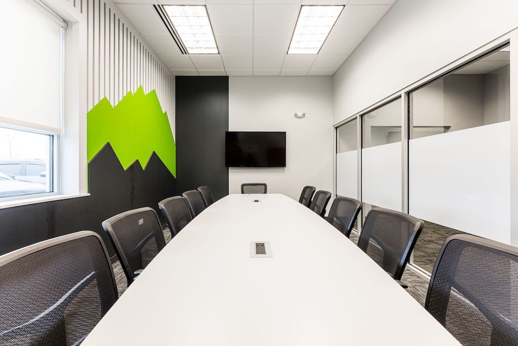 Conference room with long white table, black chairs, and a mountain design on a wall.