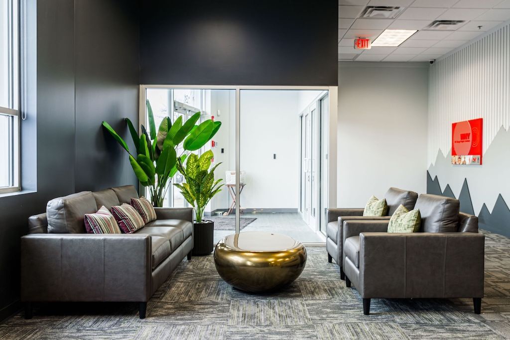 Modern office waiting area with gray leather furniture, plants, and gold coffee table.