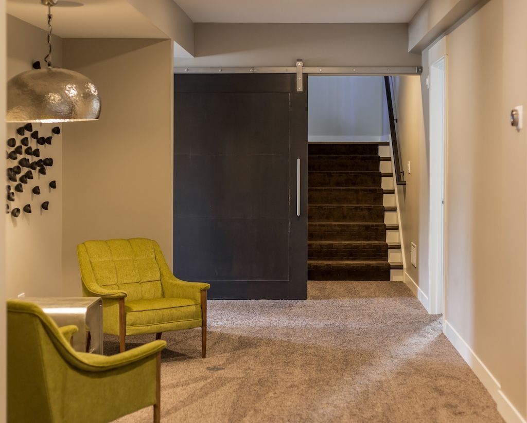 Cozy basement seating area with two green armchairs, a large sliding black door, and stairs leading upwards.