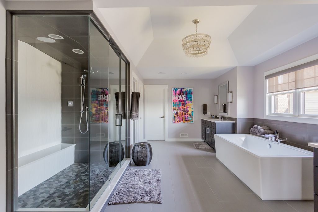 Spacious modern bathroom with glass shower, freestanding tub, artwork, and gray tile floor.