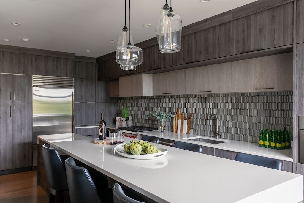 Modern kitchen with gray cabinets, white countertop island, stainless steel appliances, and pendant lights.