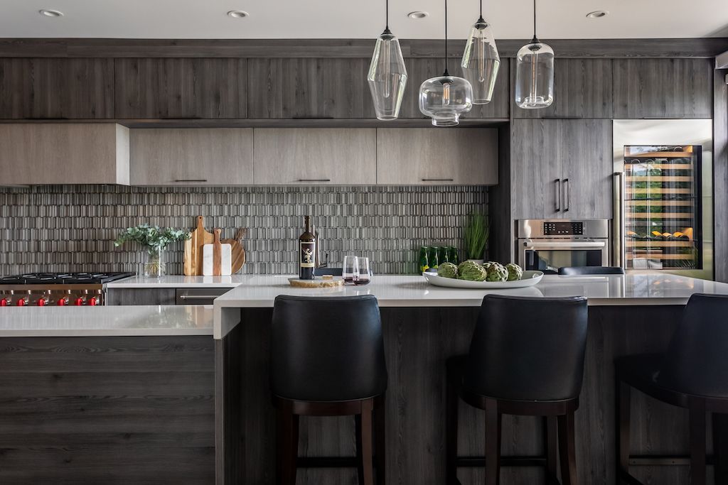Modern kitchen with bar seating, gray cabinetry, and glass pendant lights. A wine cooler is visible.