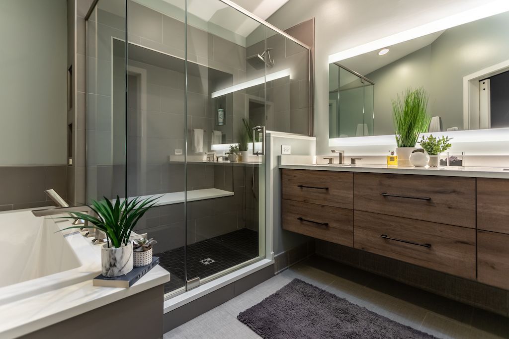 Modern bathroom with a glass shower, wooden vanity, and tub. Gray and white color scheme.