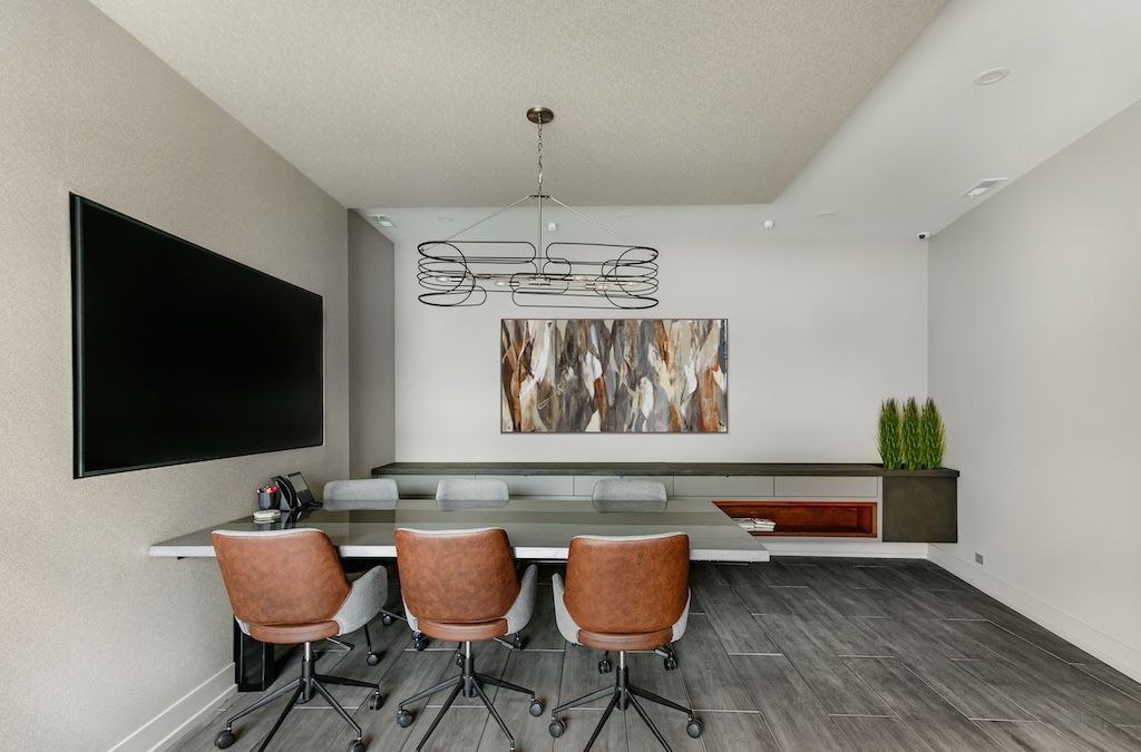 Conference room with long table, leather chairs, art, mounted screen, and contemporary lighting.