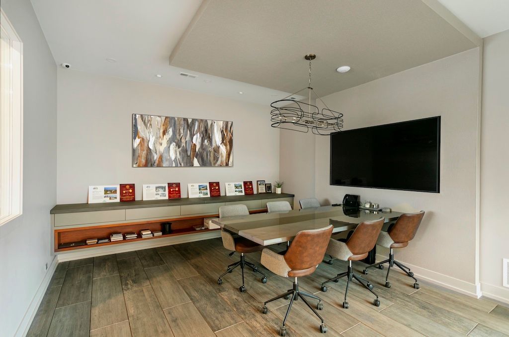 Modern conference room with large TV, long table, and chairs; neutral tones.