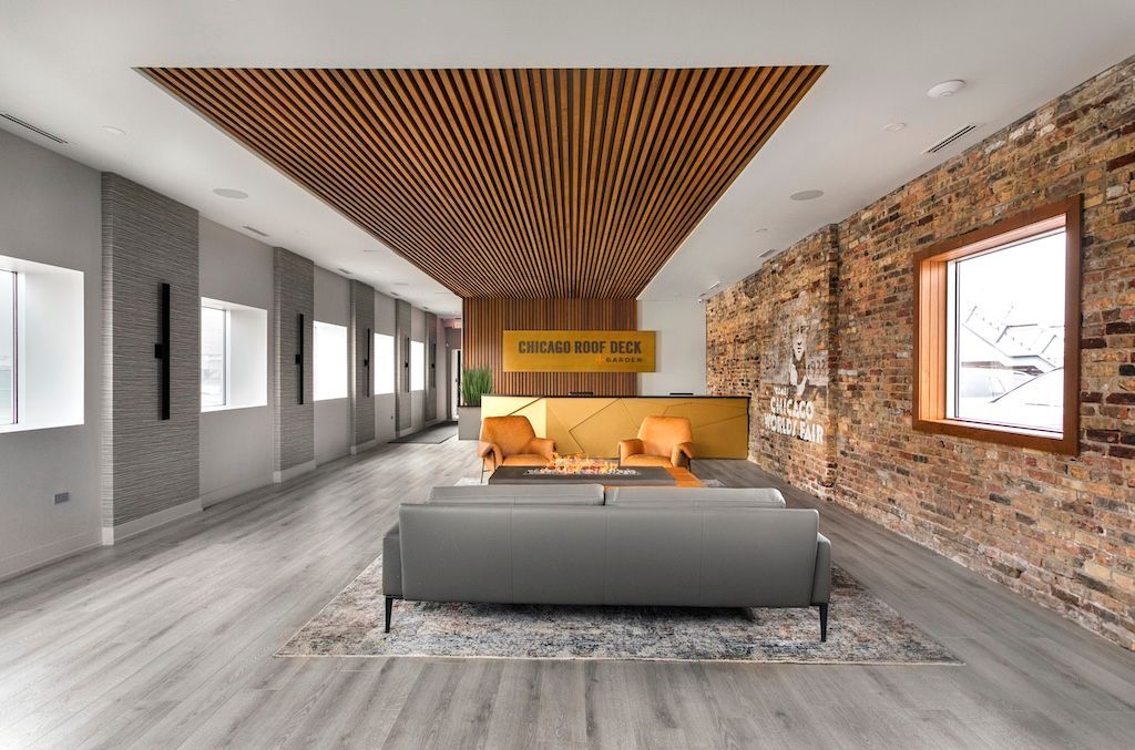Lobby with wooden slatted ceiling, brick wall, gray couch, and gold reception desk.
