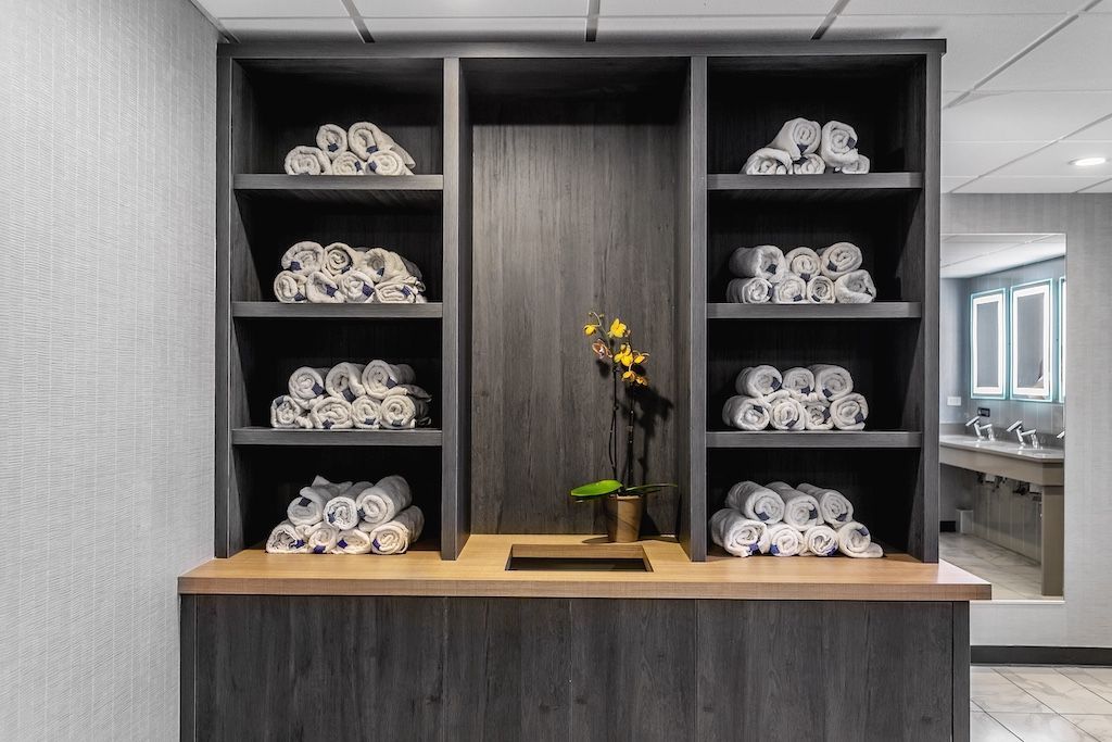 Wooden storage unit with rolled white towels on shelves, decorative orchids, and a counter.