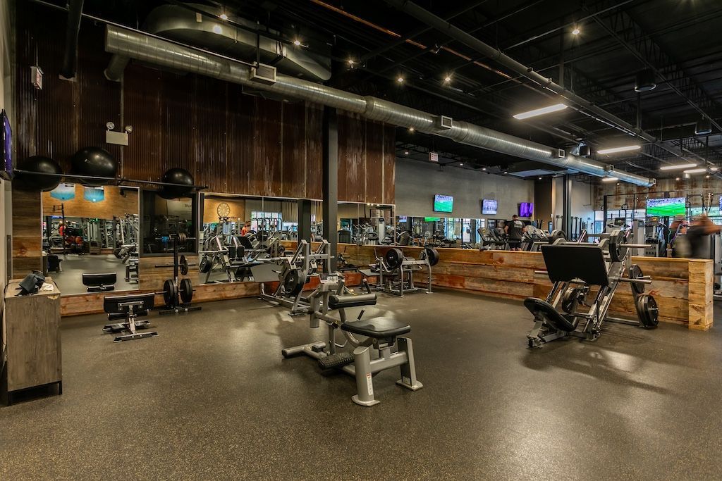 Gym interior with fitness equipment and mirrors, illuminated by overhead lights.